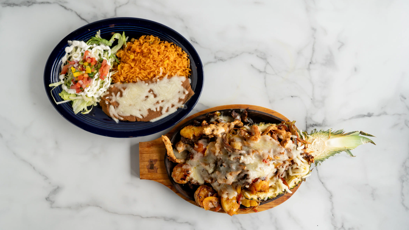 Tender grilled steak, chicken, and shrimp and pineapple served sizzling with sautéed bell peppers, onions, and tomatoes. Comes with rice, beans, lettuce, sour cream, shredded cheese, pico de gallo, an extra tomato slice, and your choice of three flour or corn tortillas