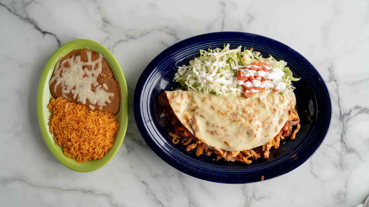 Grilled quesadilla filled with your choice of meat, bell peppers, onions, tomatoes, and cheese, covered with cheese sauce. Served with lettuce, sour cream, tomato, refried beans, and rice